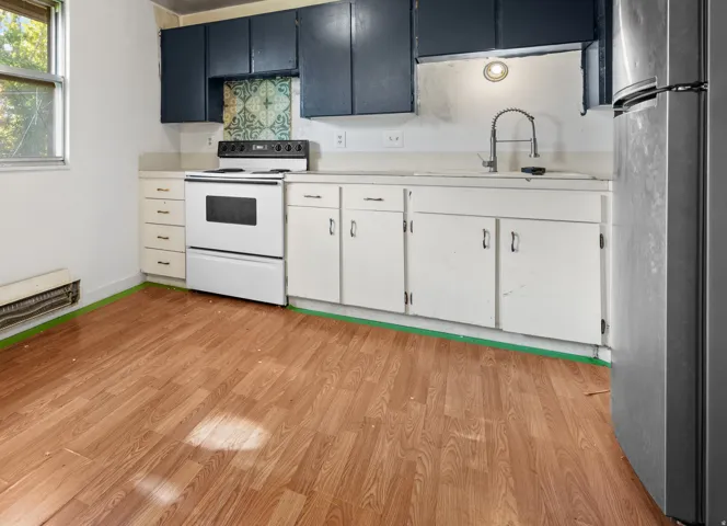 Kitchen featuring wood-finish flooring, white cabinetry, dark blue upper cabinets, a white range, and a window