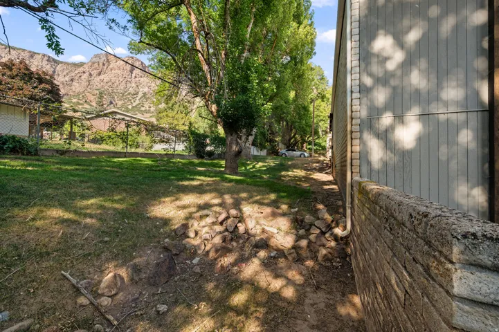 Expansive outdoor space featuring a stone retention wall, mature trees, and natural landscaping with mountain scenery