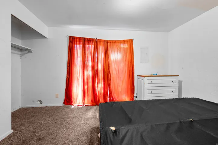 Carpeted room with white walls and an open closet space featuring a single shelf and hanging rod