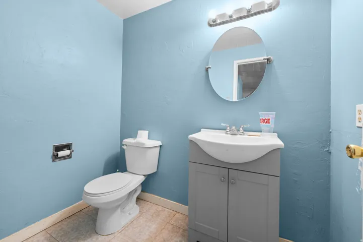 Bathroom featuring a gray vanity with an integrated sink, a circular mirror, and an overhead light fixture