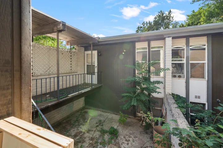 Covered outdoor patio with a black iron railing, wood slat ceiling, and an exterior door