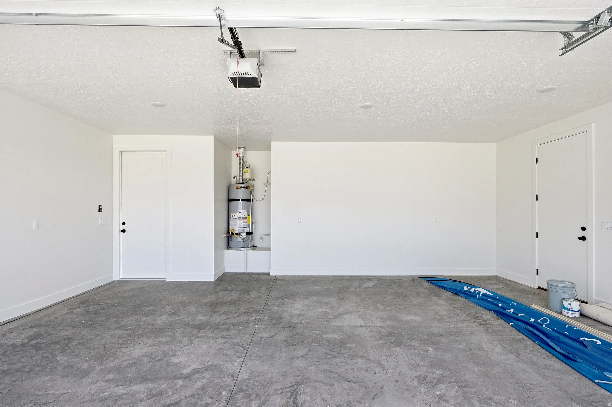 Spacious garage with a concrete floor, two entry doors, and a visible water heater installation
