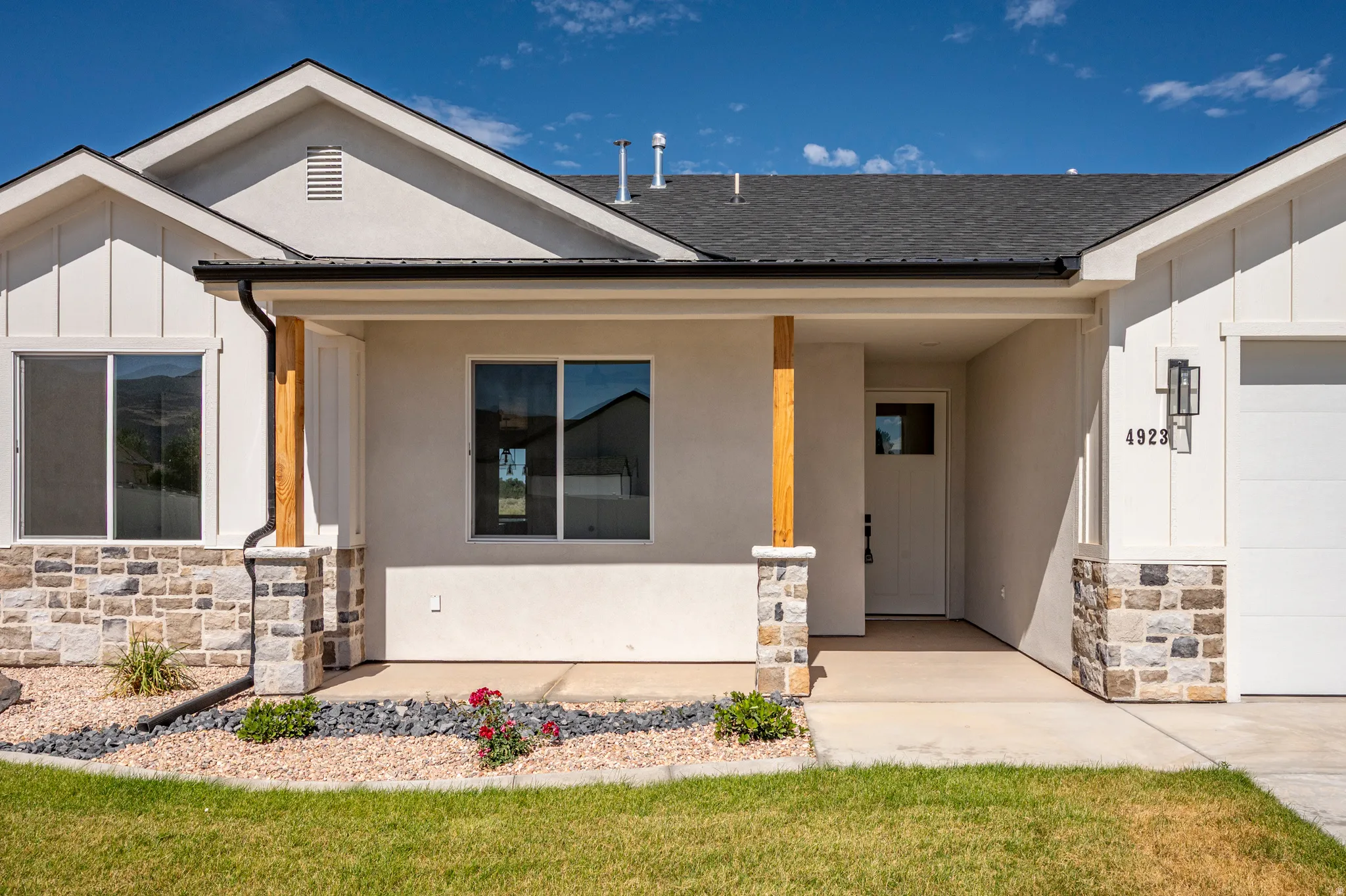 Contemporary exterior featuring a covered entry, stone veneer accents, stucco siding, and board and batten details