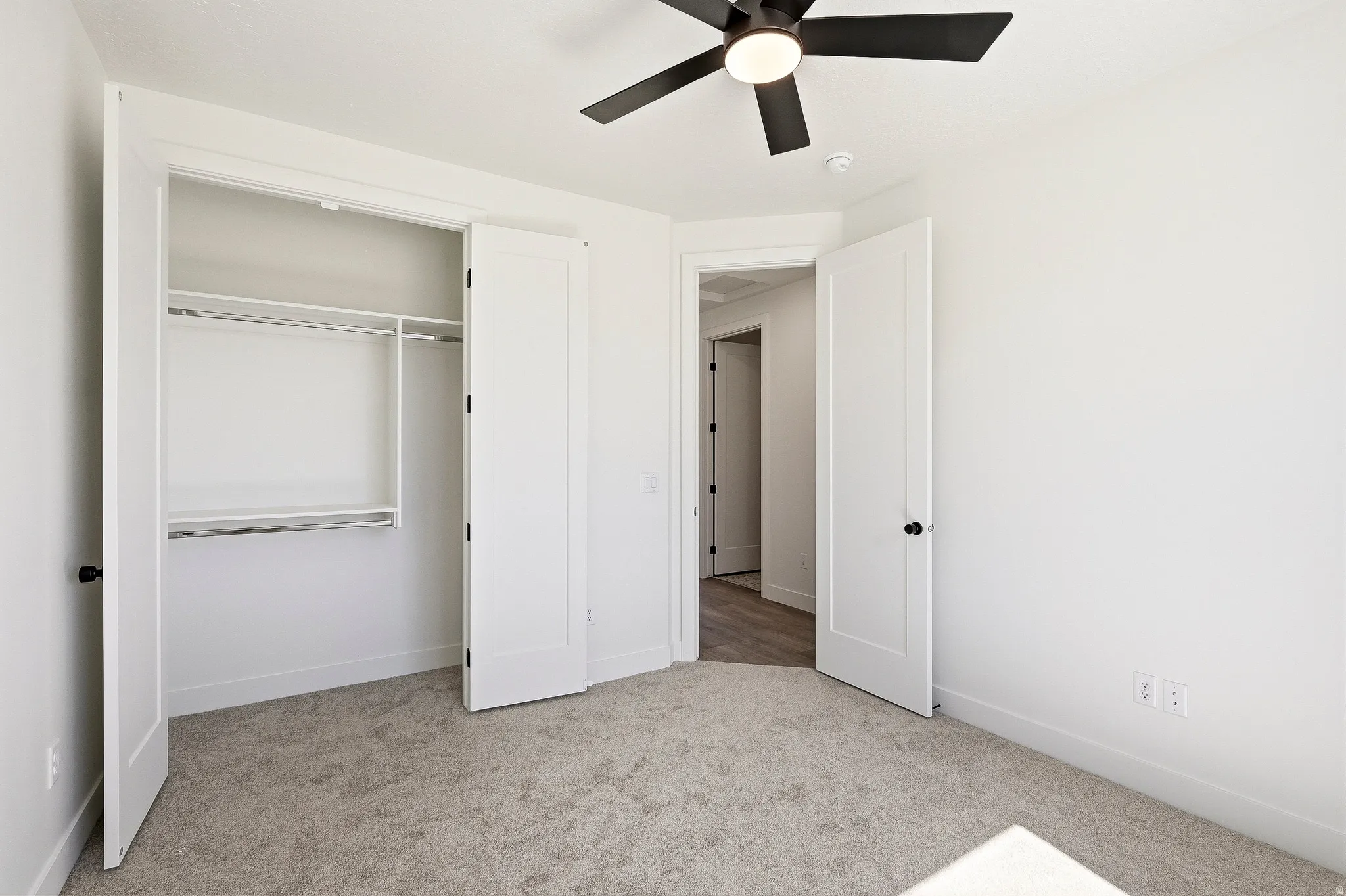 Carpeted room featuring a built-in closet with shelving and hanging rods, a ceiling fan, and white doors with matte black hardware
