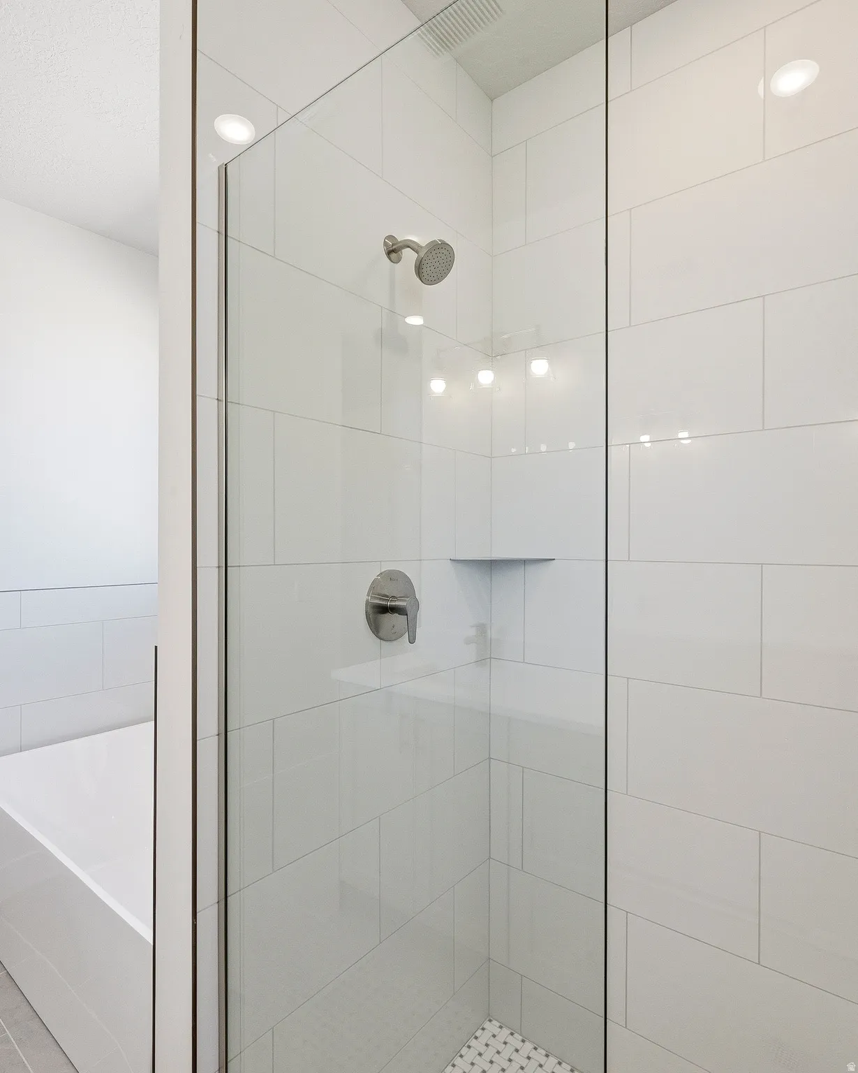 Glass-enclosed shower with subway tile surround, recessed lighting, chrome fixtures, and a built-in corner shelf