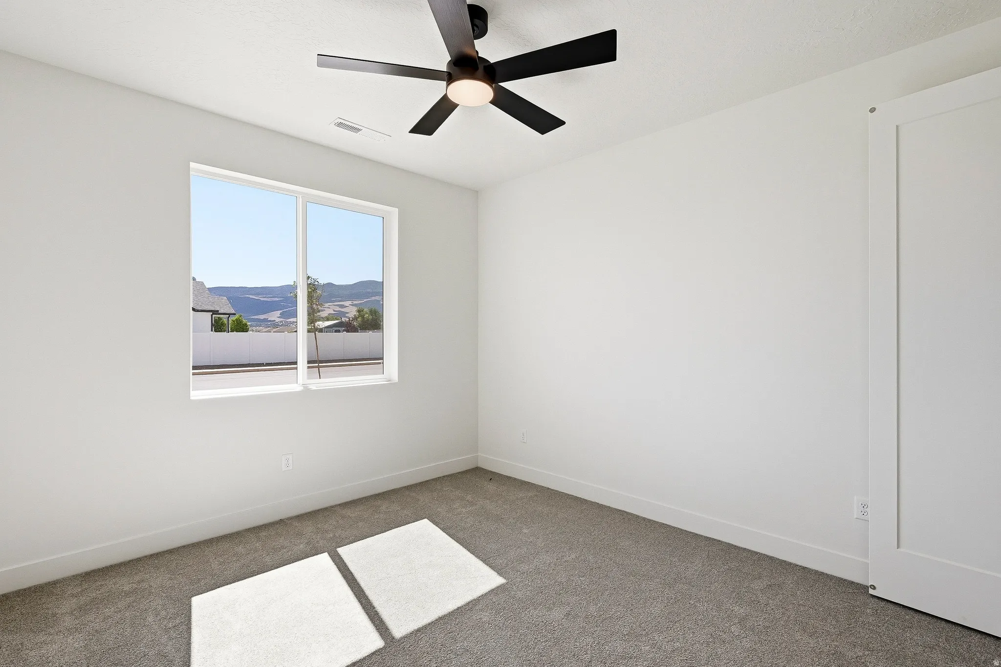 Bright interior space featuring a large window, dark gray carpeting, and a modern ceiling fan with integrated lighting