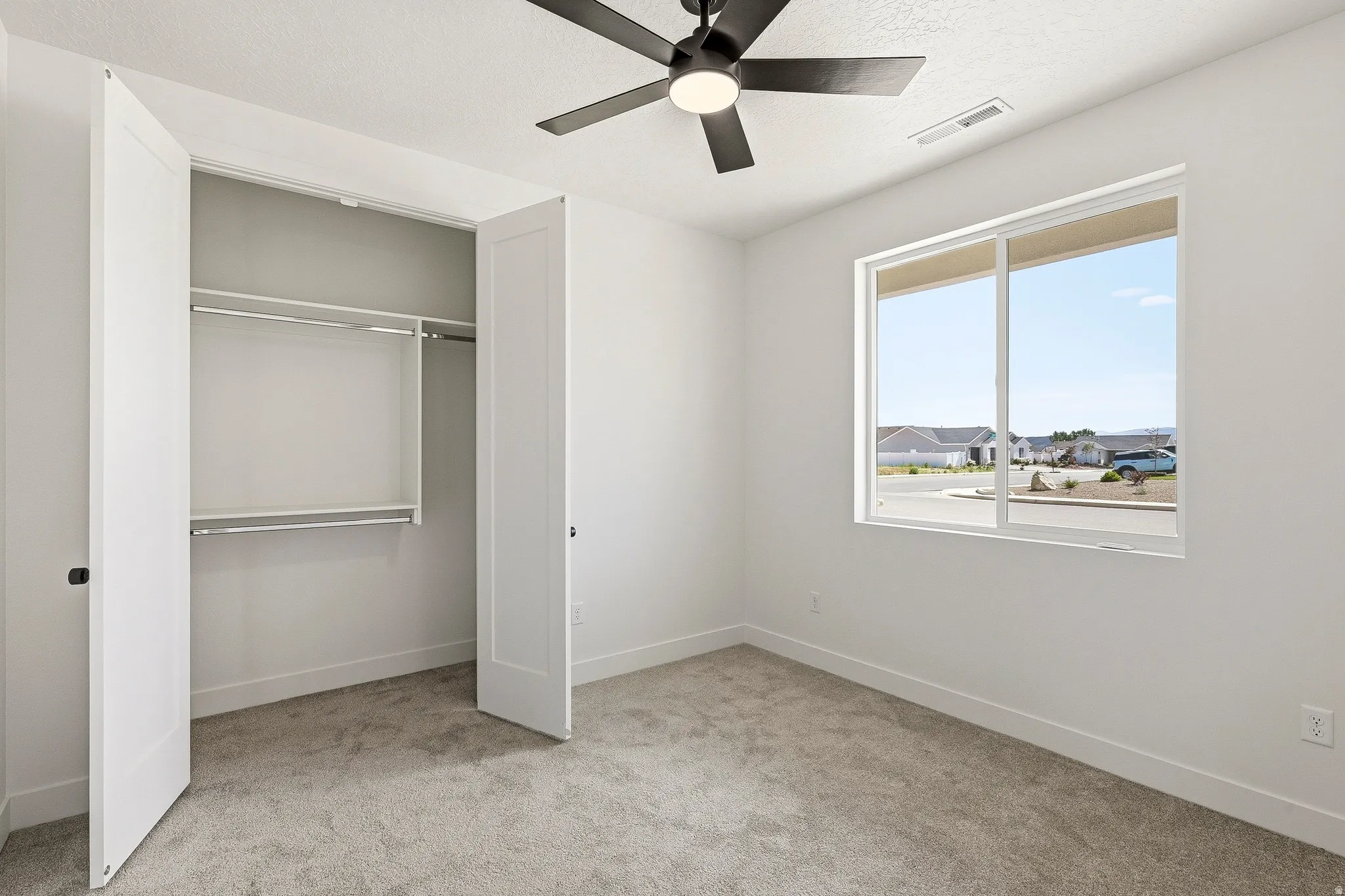 Bedroom featuring light gray carpet, a ceiling fan with integrated lighting, and a double-pane window