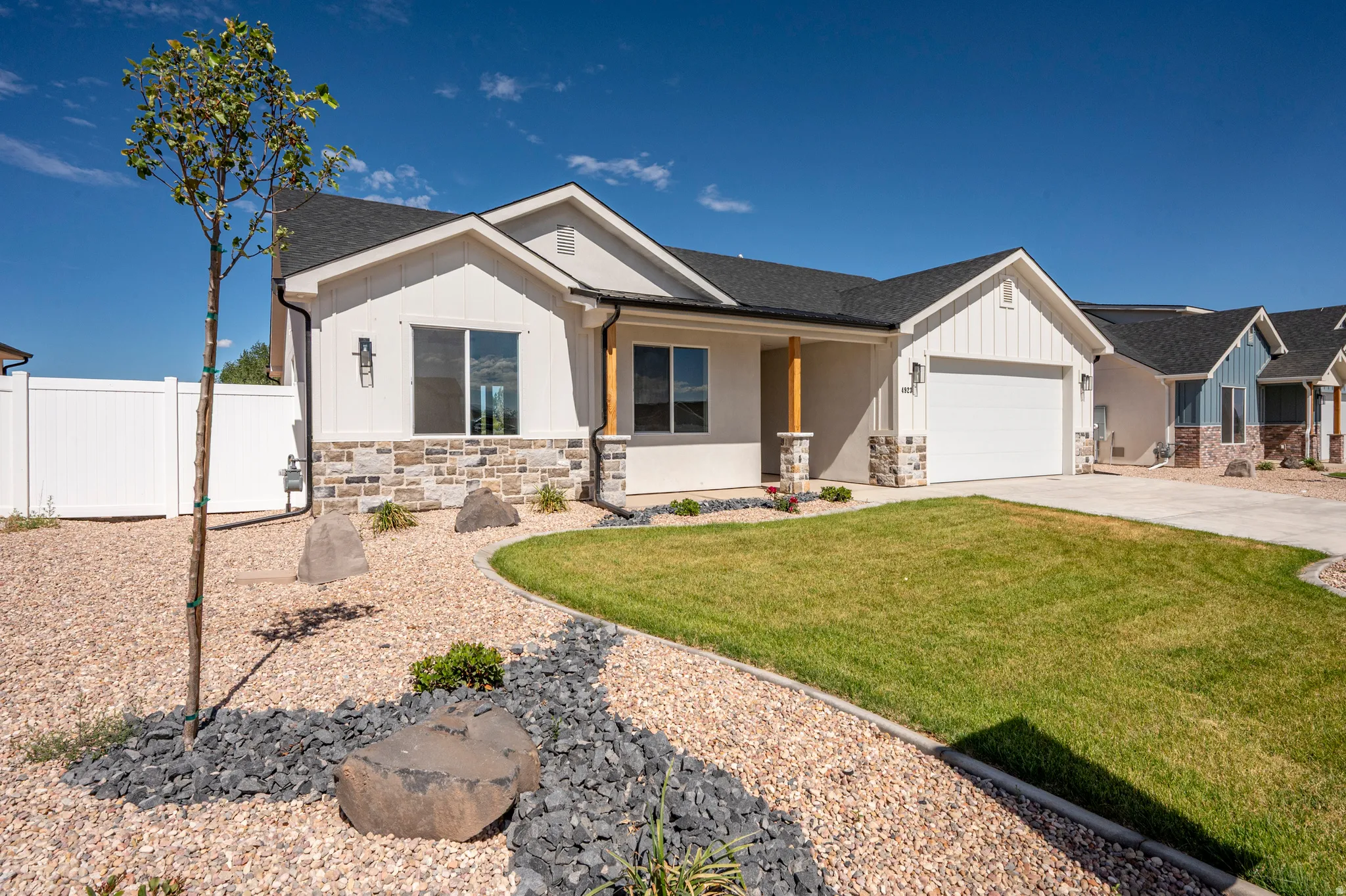 Contemporary ranch-style exterior featuring a white stucco finish, board-and-batten gables, and a stone veneer foundation
