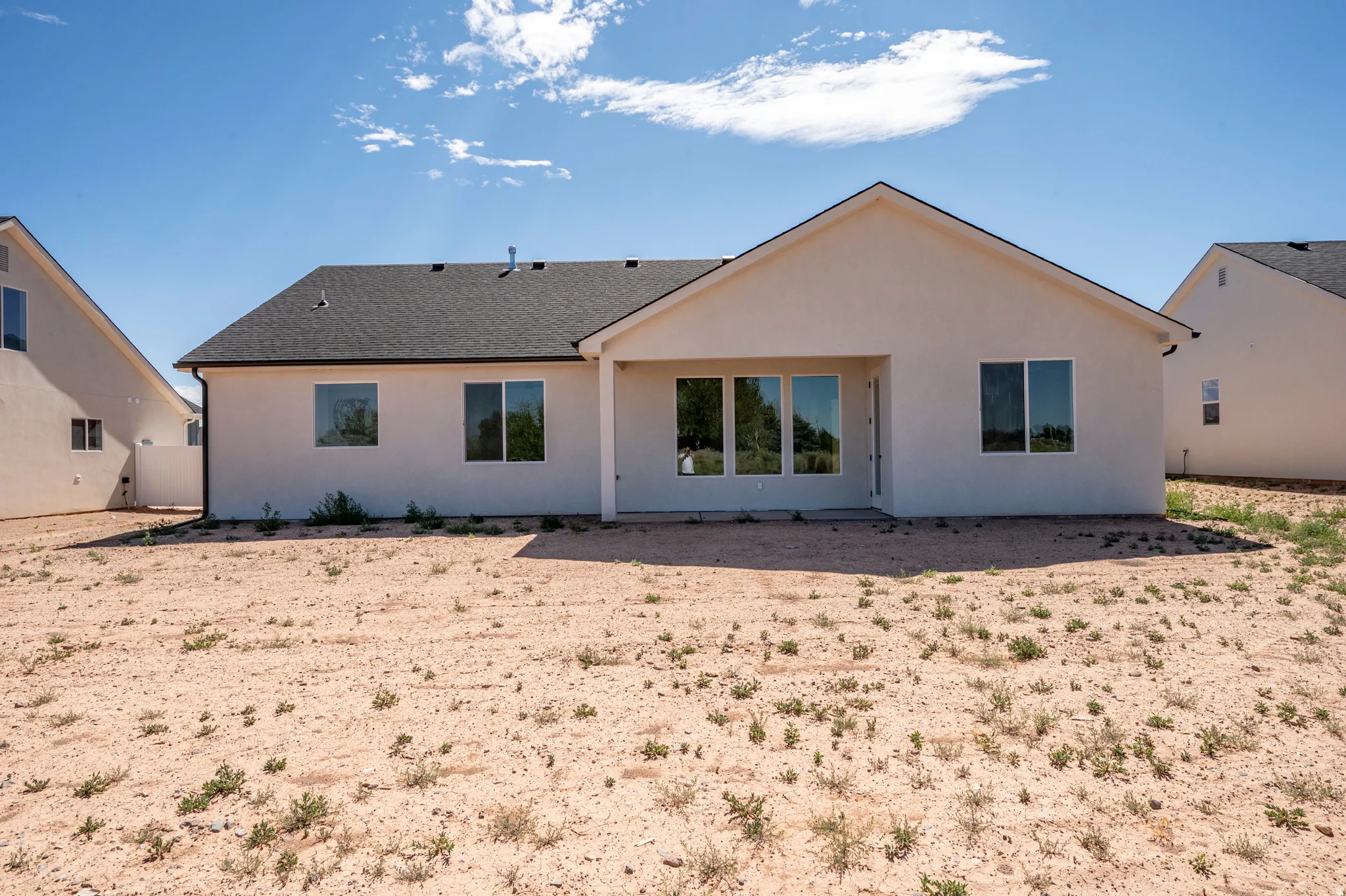 Rear exterior showcasing a neutral stucco finish, multiple windows, a covered patio area, and a dark shingle roof