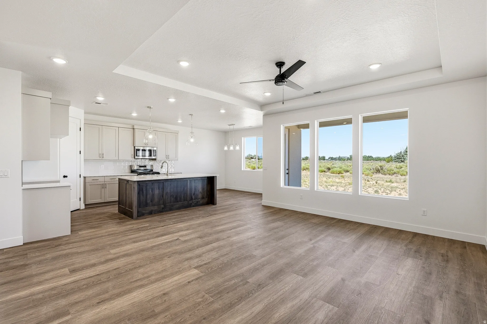 Expansive open-concept living area featuring wood-finish flooring and a tray ceiling with recessed lighting