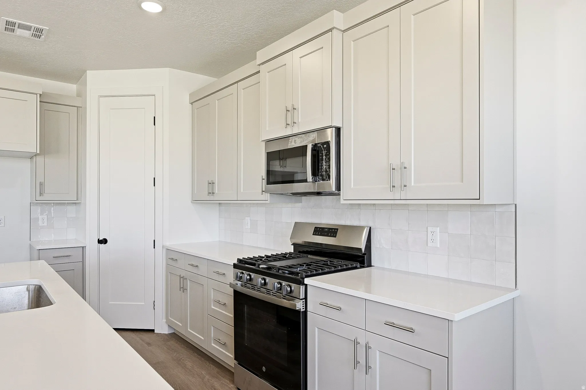 Modern kitchen featuring light gray cabinetry, stainless steel appliances, white countertops, and a subway tile backsplash
