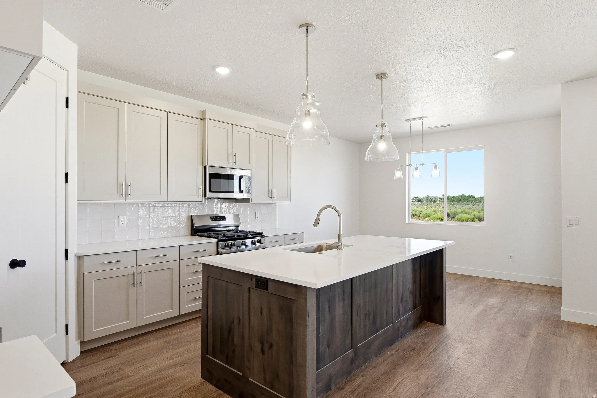 Open-concept kitchen featuring an oversized island with an integrated sink, light-toned cabinetry, stainless steel appliances, and wood-finish flooring