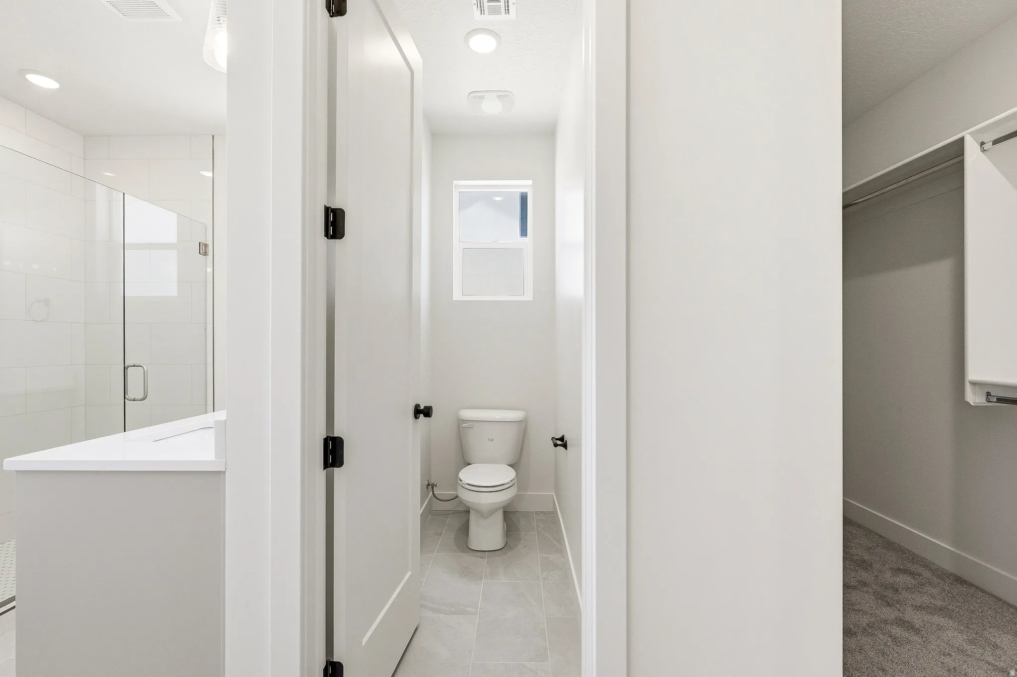 Modern bathroom featuring a separate water closet with a window, a glass-enclosed shower, a vanity with a white countertop, and recessed lighting
