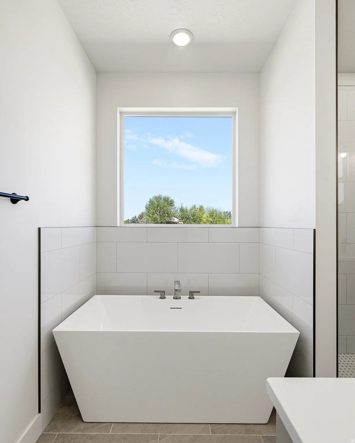 Freestanding soaking tub with chrome fixtures, set against a backdrop of white subway tile wainscoting and a large window