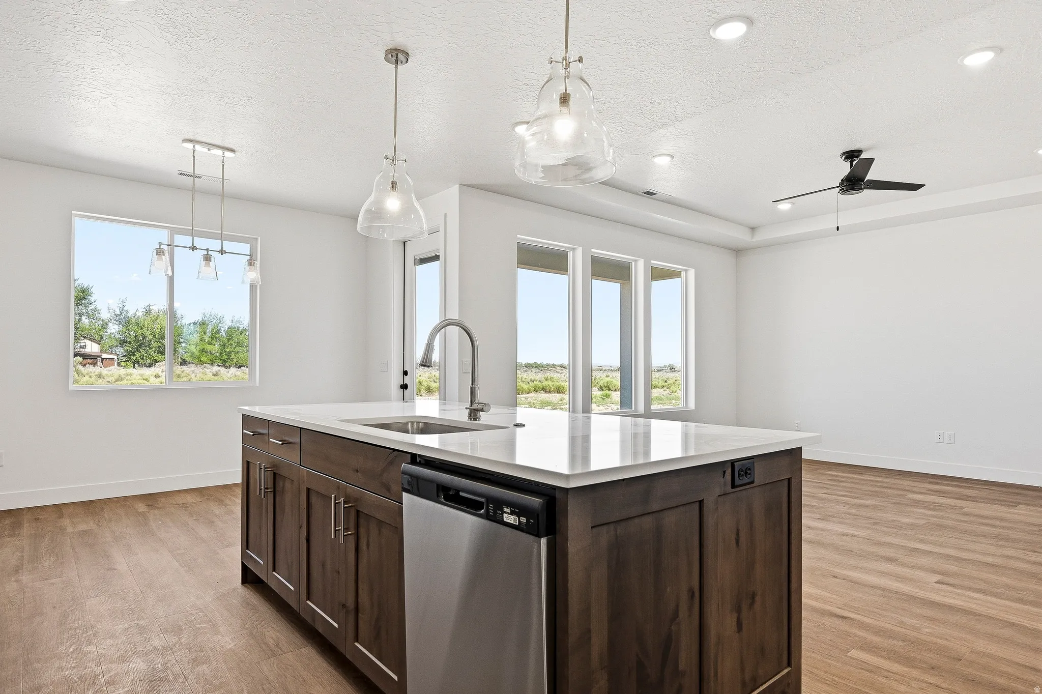 Kitchen island with a white countertop and wood-finish cabinetry, featuring a built-in sink and stainless-steel dishwasher