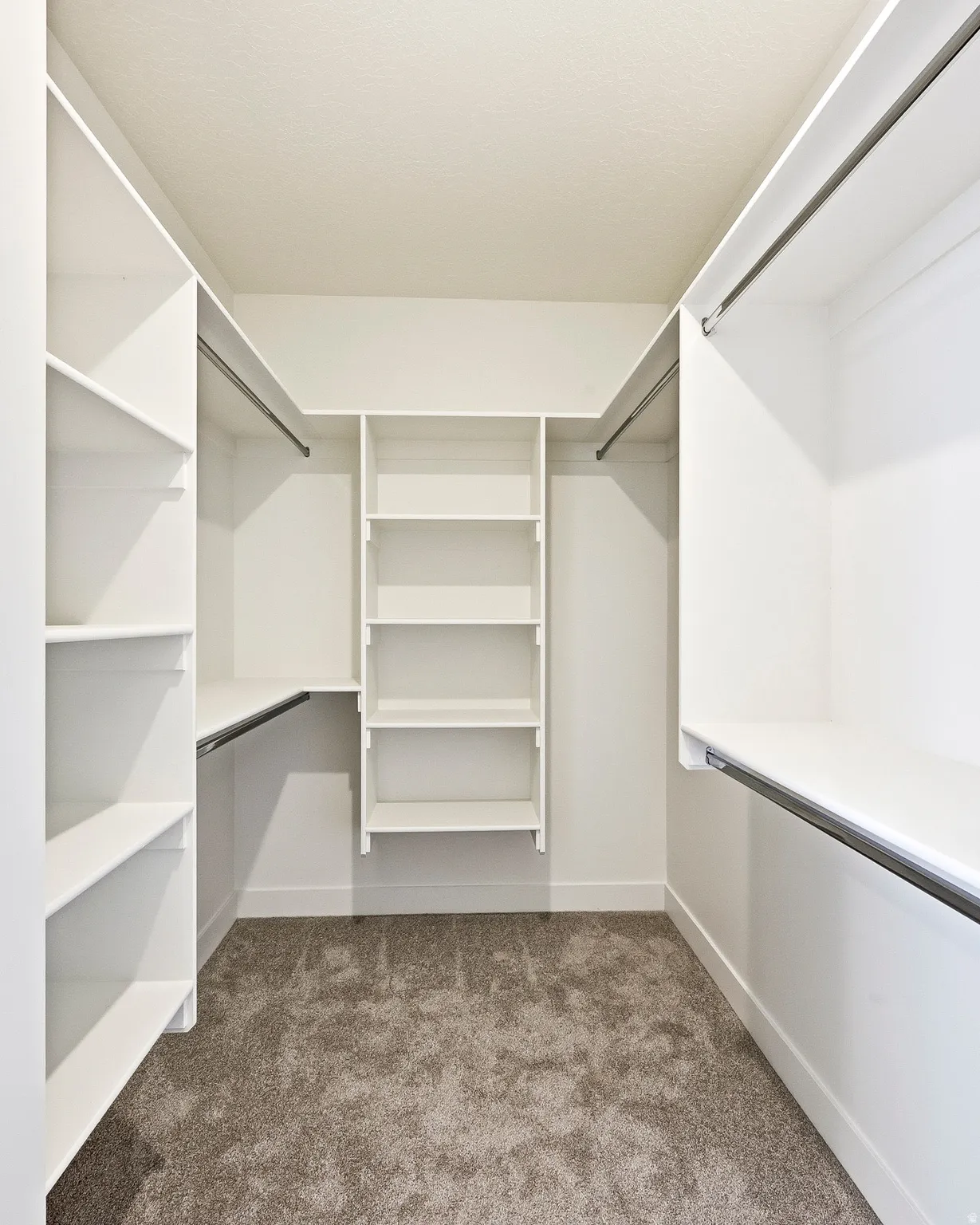 U-shaped closet system featuring white shelving units, multiple hanging rods, and textured carpeting
