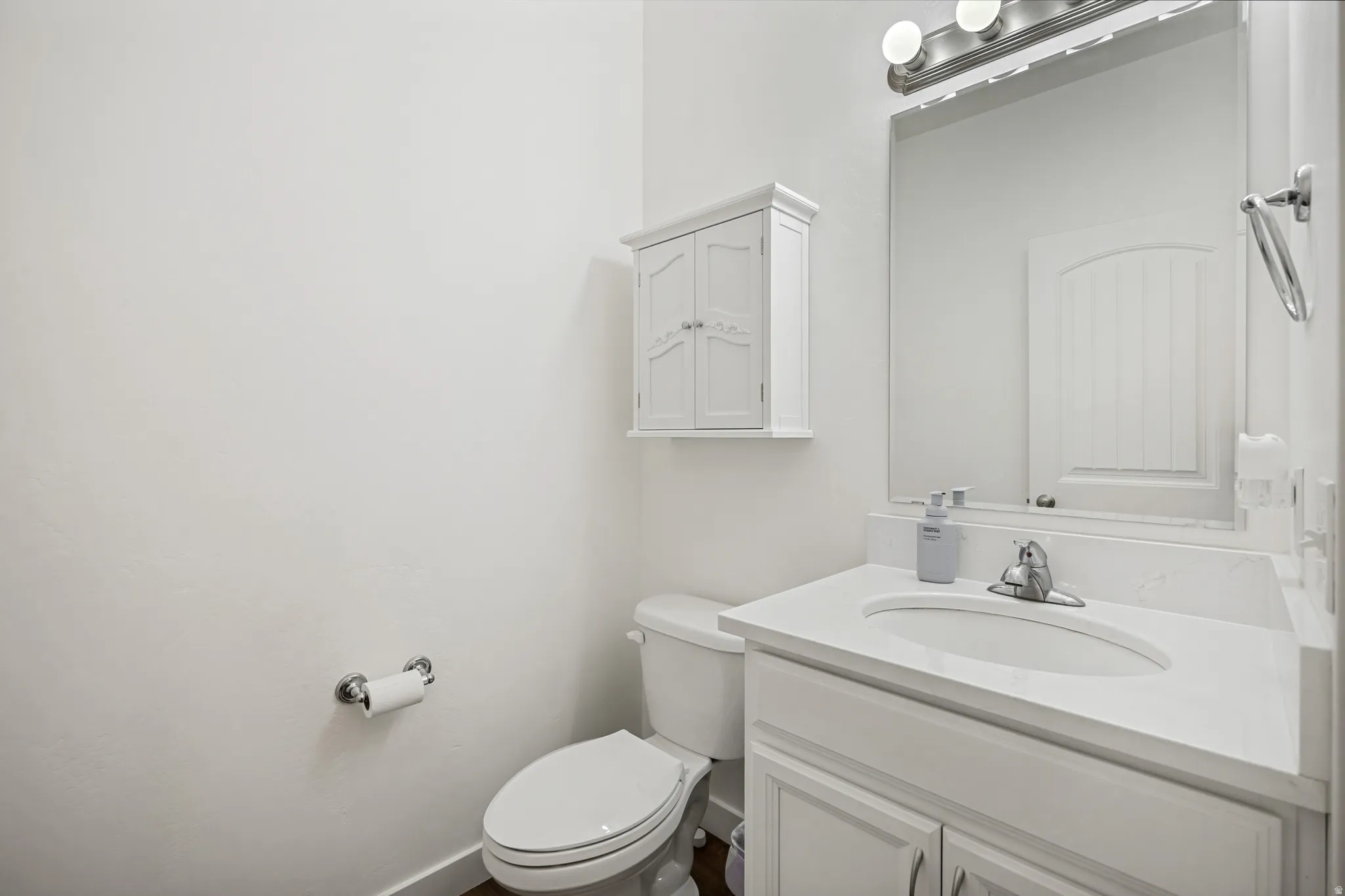 Bathroom featuring a white vanity with an integrated sink and countertop, chrome faucet, and a wall-mounted mirror with a three-bulb light fixture