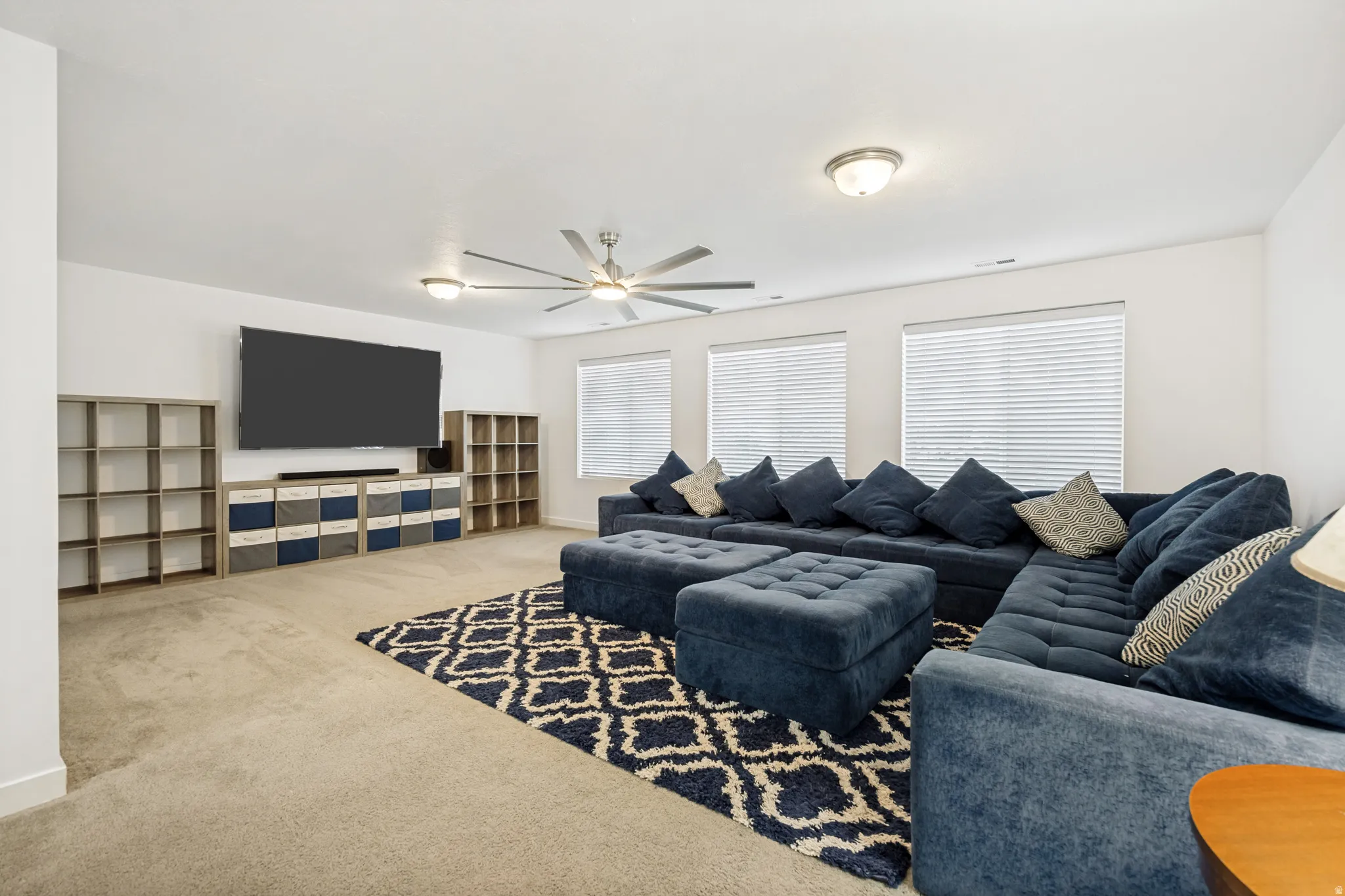 Spacious room featuring light-colored carpeting, a ceiling fan with integrated lighting, and multiple windows with blinds