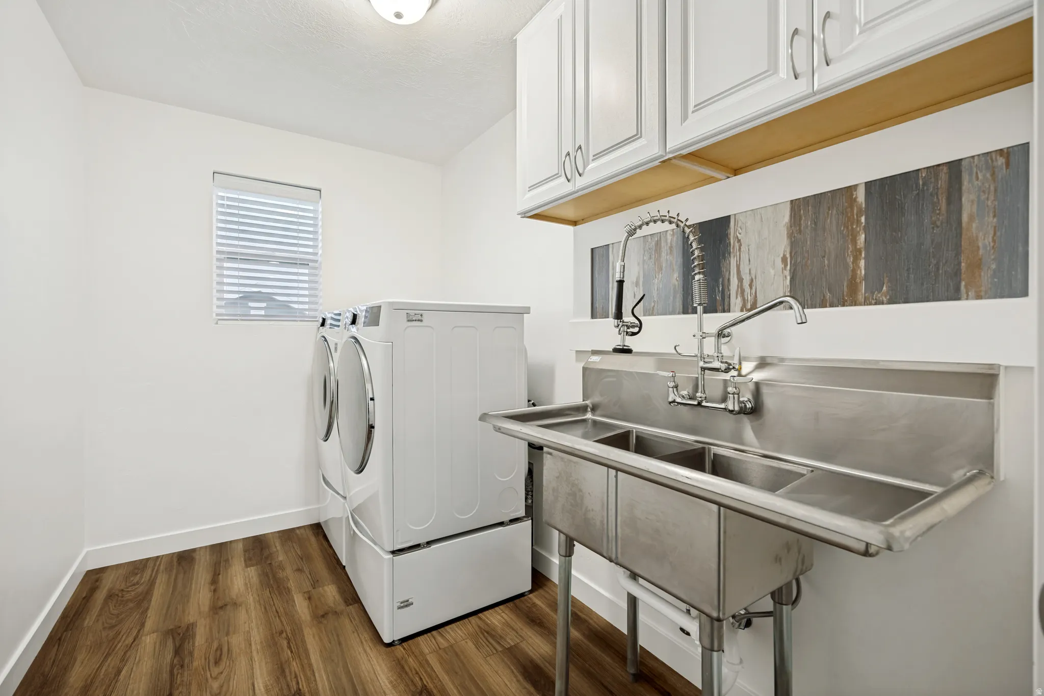 Laundry room featuring wood-finish flooring, a utility sink with dual faucets, and upper cabinetry