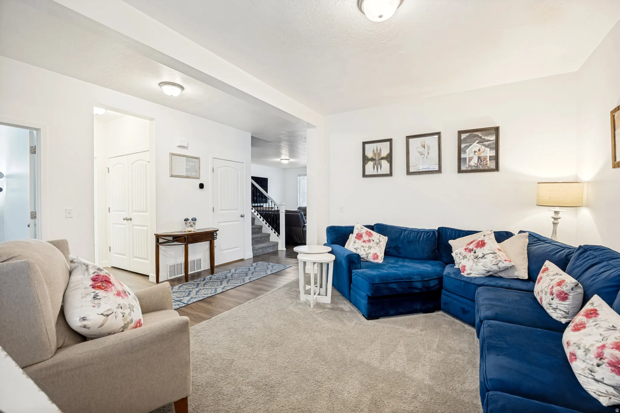 Carpeted living area featuring white walls and ceiling, recessed lighting, and wood-finish flooring extending into the entry