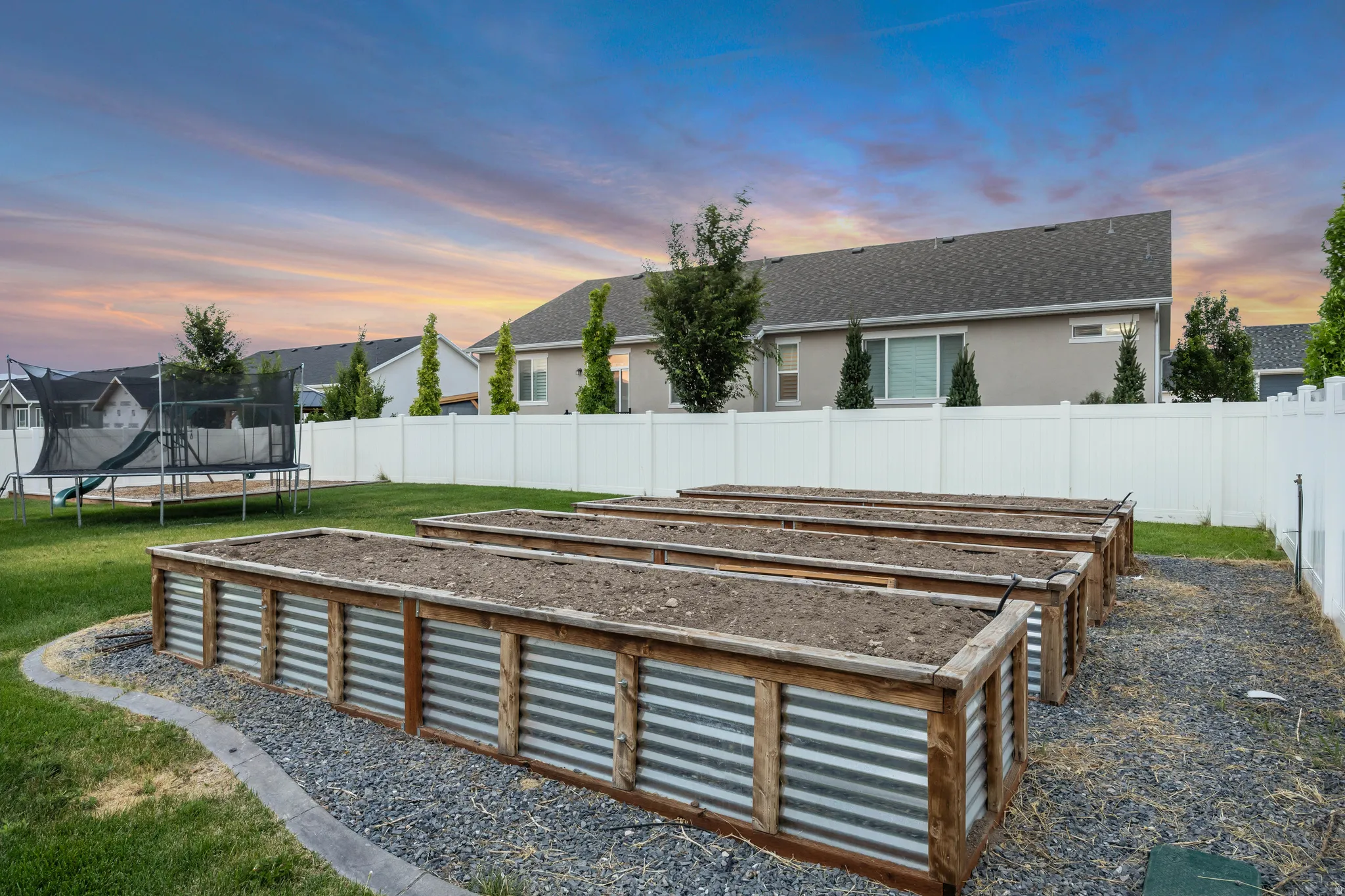 Backyard featuring multiple raised garden beds with wood and corrugated metal construction, surrounded by pea gravel