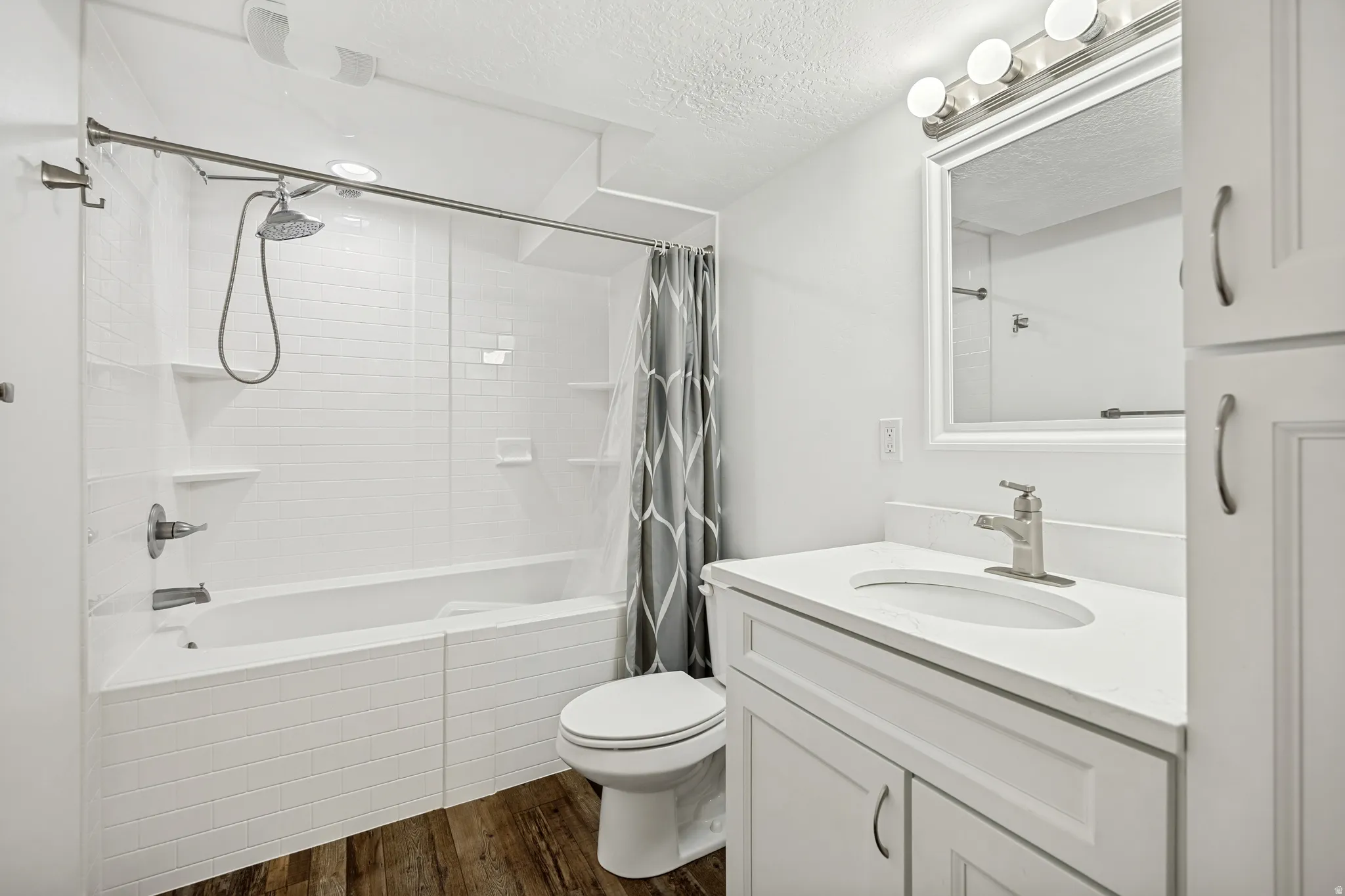 Bathroom featuring a white subway tile tub surround, white vanity with integrated sink, white countertop, and wood-finish flooring