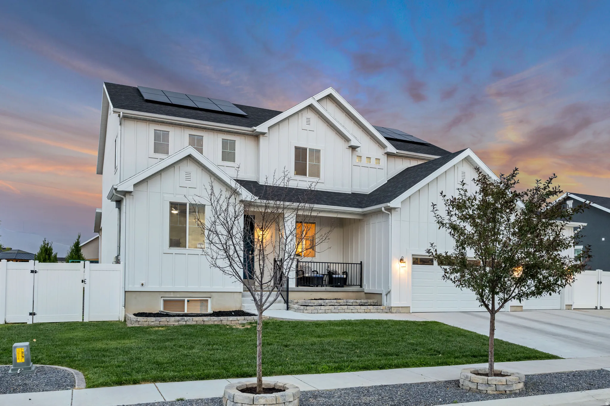 Modern farmhouse exterior featuring white board-and-batten siding, a dark shingle roof, solar panels, and an attached garage