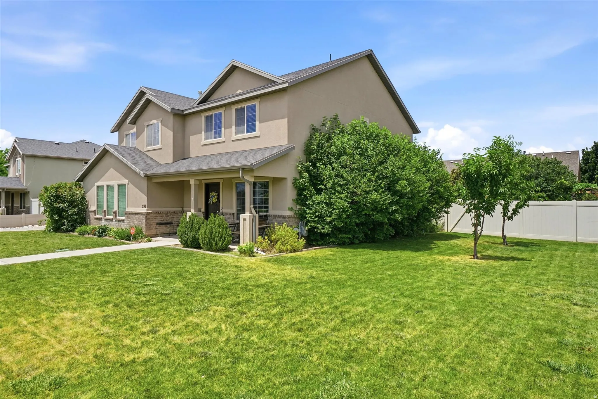 Two-story stucco residence featuring a covered front porch, stone accent siding, and a gabled roofline