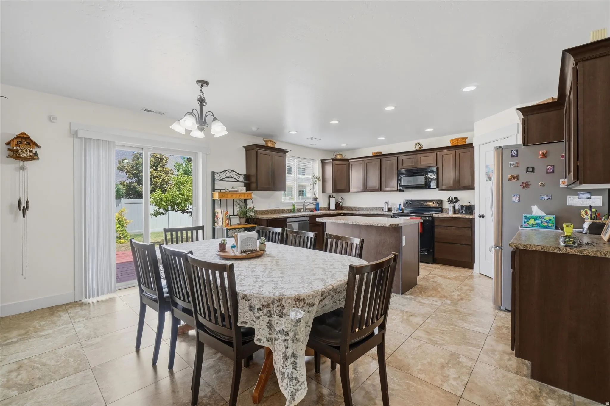 Open-concept kitchen and dining area featuring tile flooring, dark wood cabinetry, a central island, and a sliding glass door providing access to the backyard