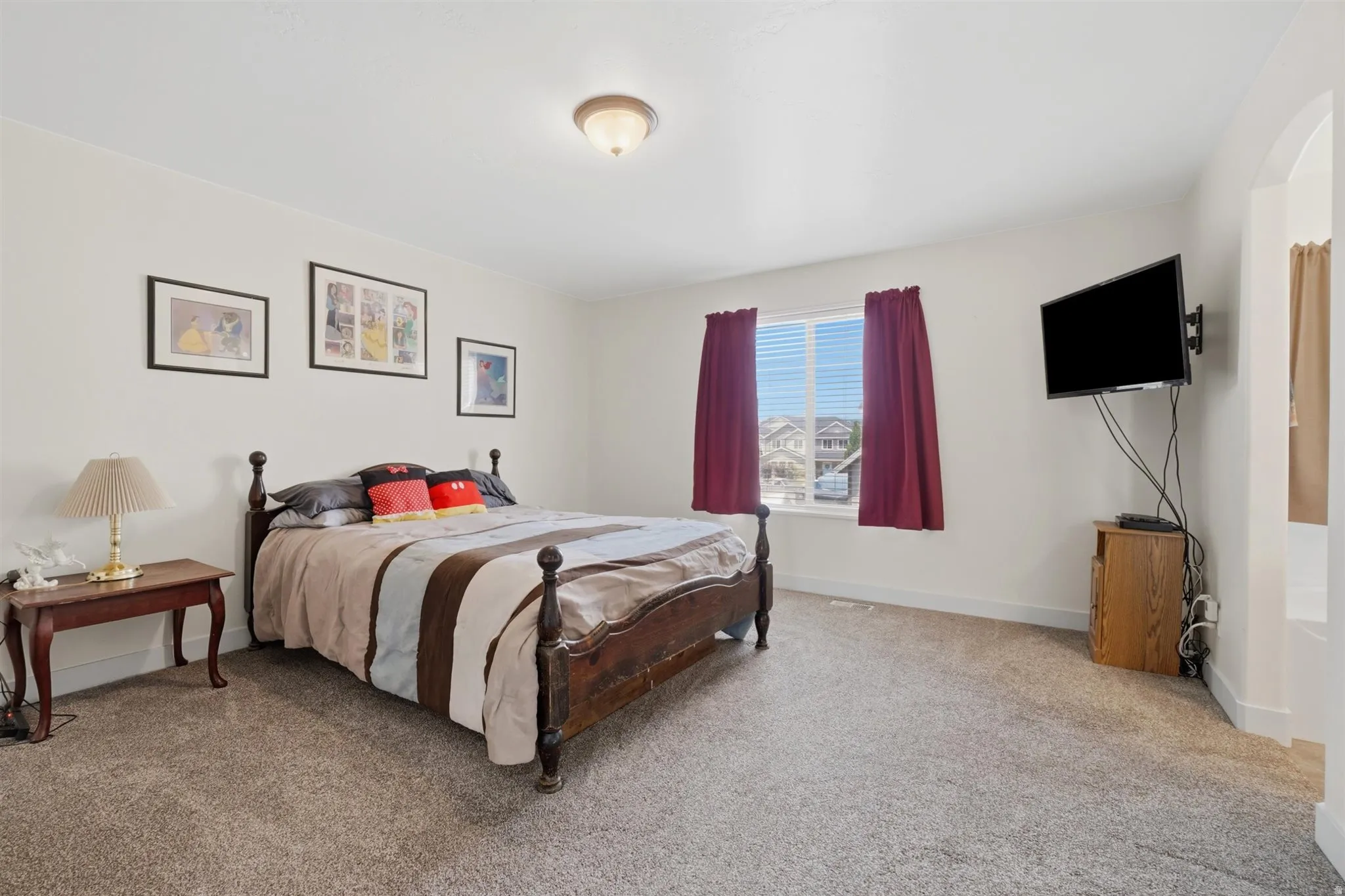 Spacious carpeted room featuring a ceiling-mounted light fixture, a window with horizontal blinds, and an arched doorway