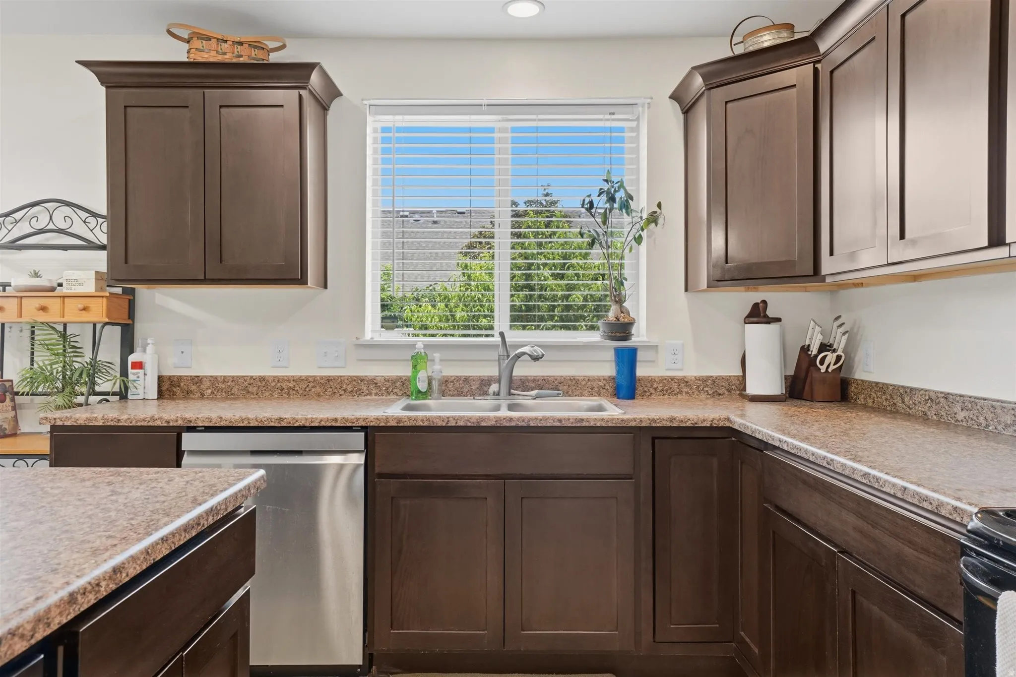 Kitchen featuring dark wood cabinetry, a stainless steel sink, speckled laminate countertops, and a built-in stainless steel dishwasher