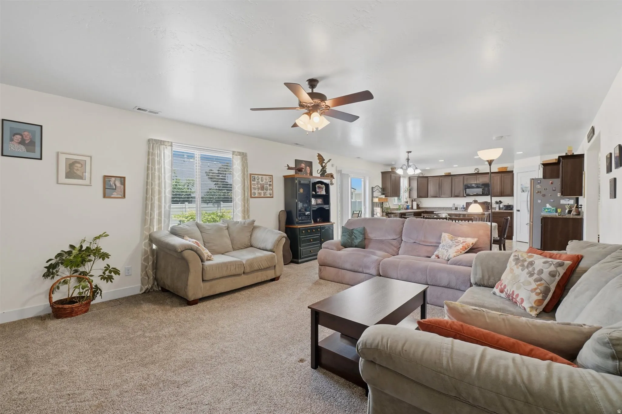 Open-concept living area with neutral carpeting, a ceiling fan, and a window with blinds