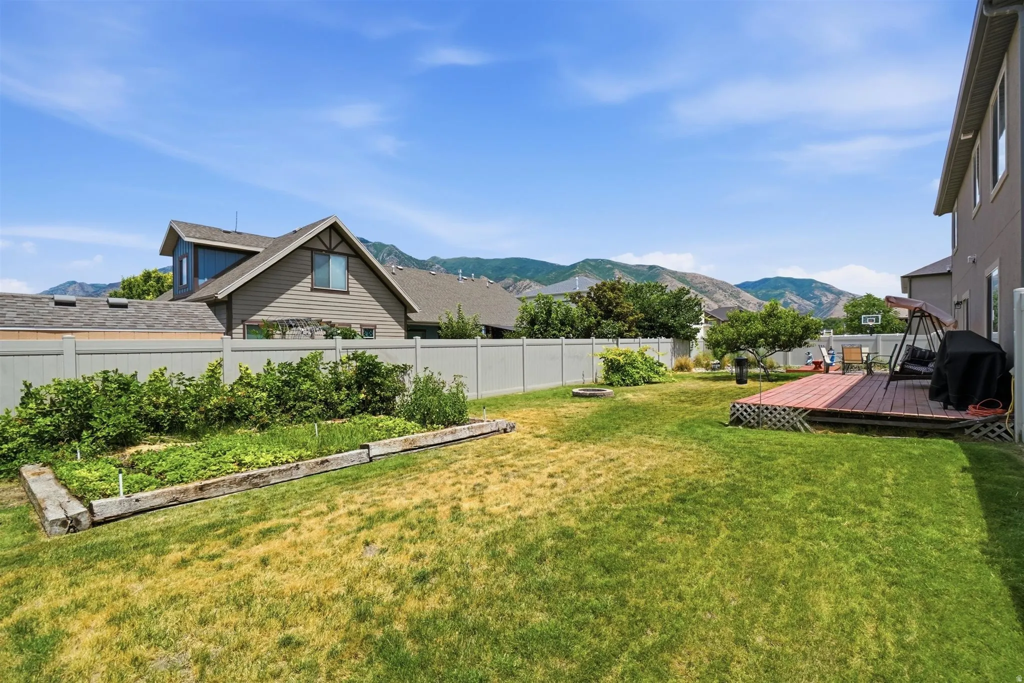 Spacious backyard featuring a wood deck, manicured lawn, and raised garden beds