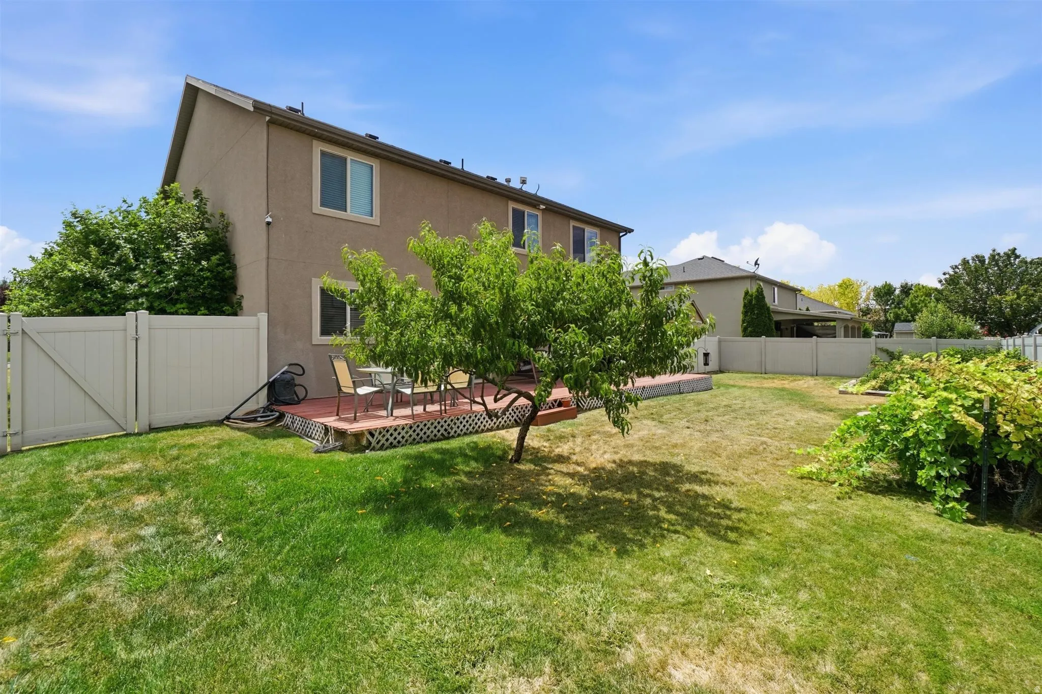 Expansive backyard featuring a manicured lawn, full privacy fencing, and a dedicated wood deck patio