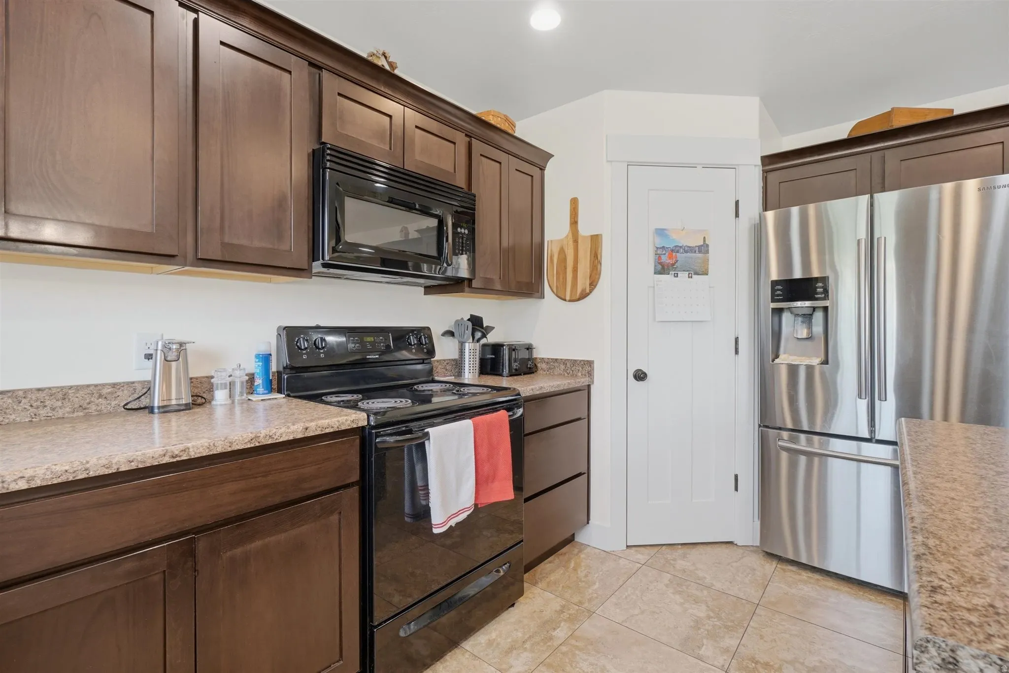 Kitchen featuring dark wood cabinetry, a stainless steel refrigerator, black range, and an over-the-range microwave