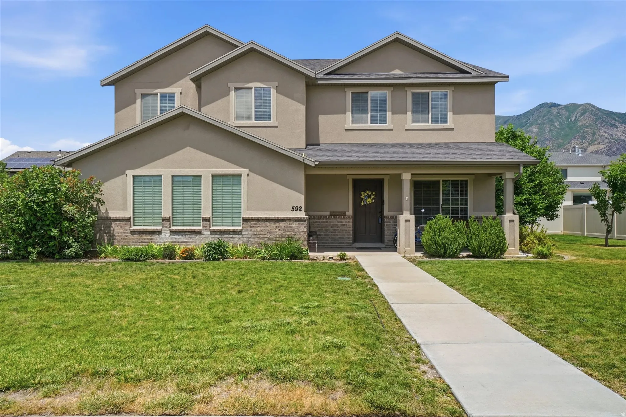 Two-story stucco and brick exterior featuring a covered front porch, a concrete walkway, and a manicured lawn