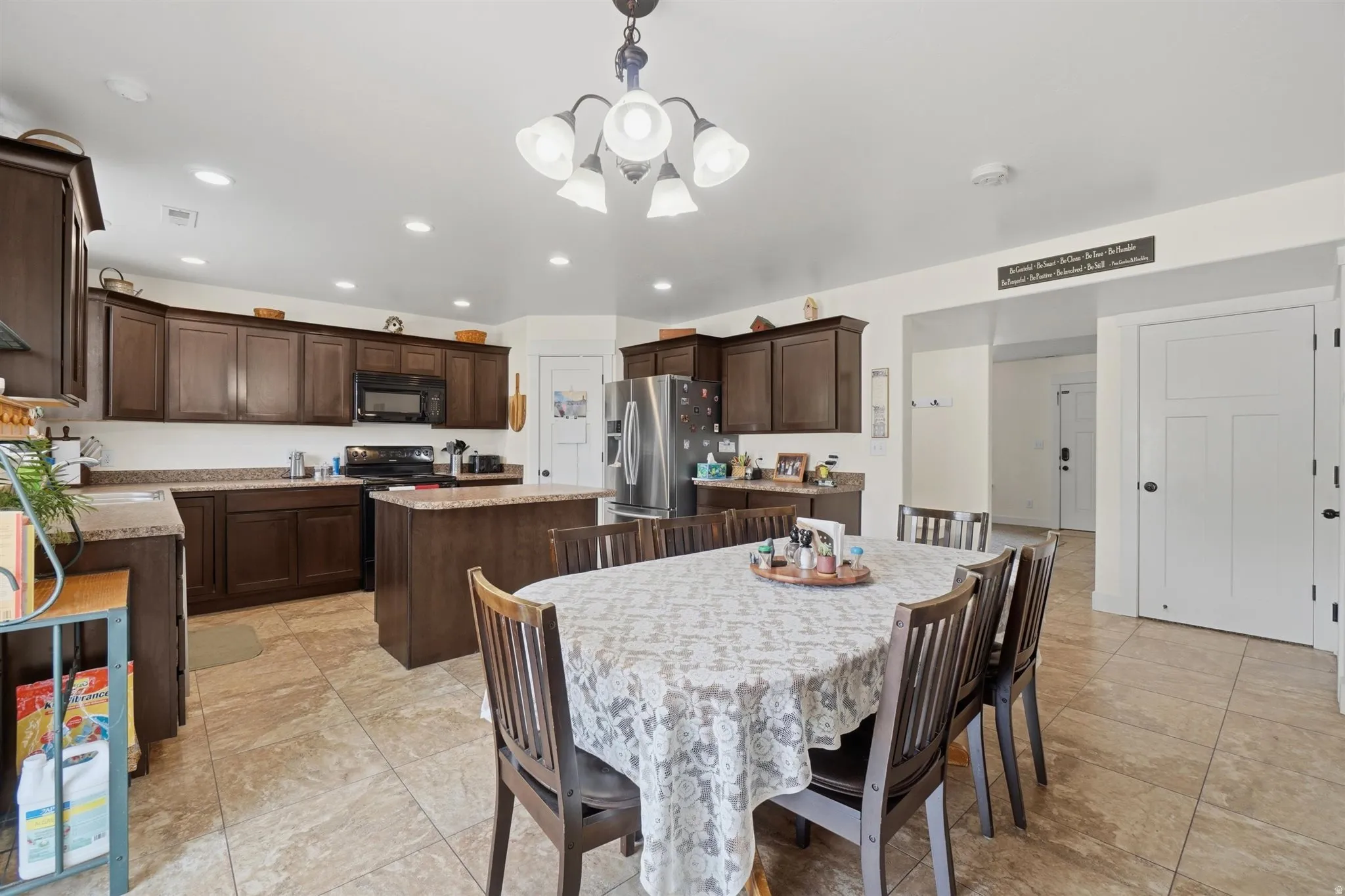 Spacious kitchen with a central dining area, featuring extensive dark wood cabinetry, granite-style countertops, stainless steel appliances, and large format tile flooring