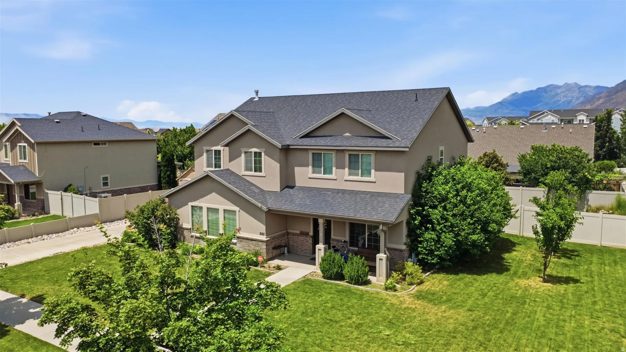 Two-story residence featuring a gray shingle roof, neutral stucco siding, and stone accents on the lower level