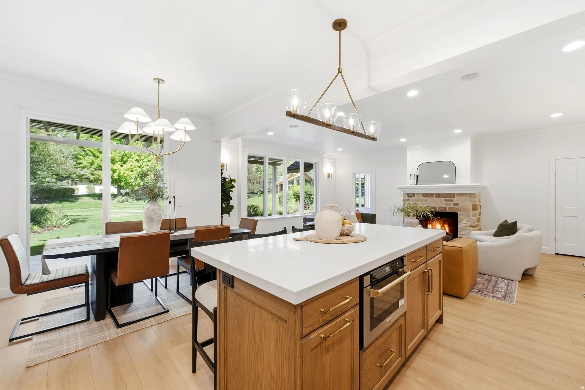 Hardwood-style flooring, a stone-clad fireplace, a kitchen island with integrated appliances, and extensive natural light