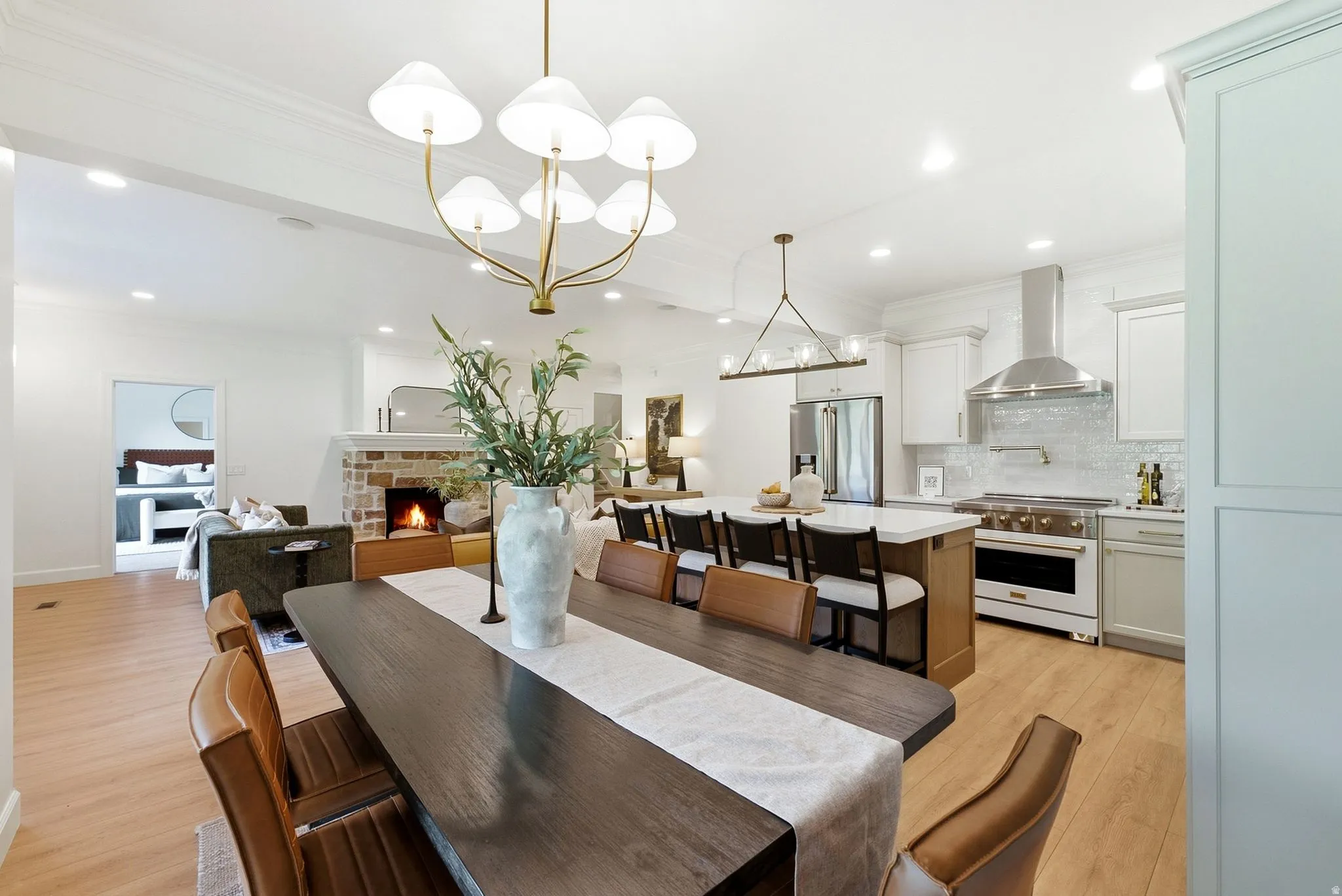 Open-concept living area featuring a kitchen with stainless steel appliances, a center island with seating, wood-finish flooring, and a brick-finish fireplace