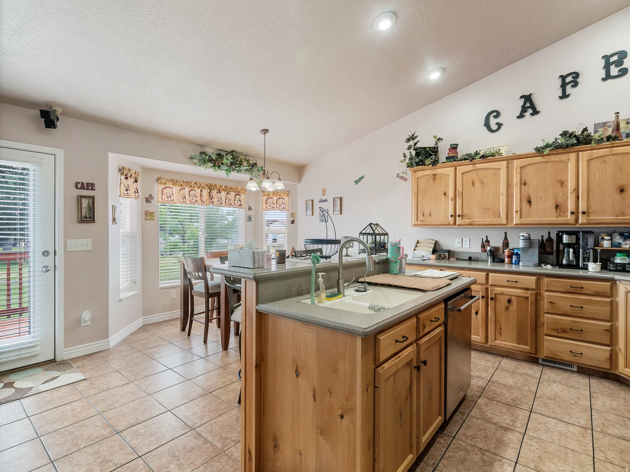 Kitchen featuring wood cabinetry, a center island with a sink, a built-in dishwasher, and a bay window dining area
