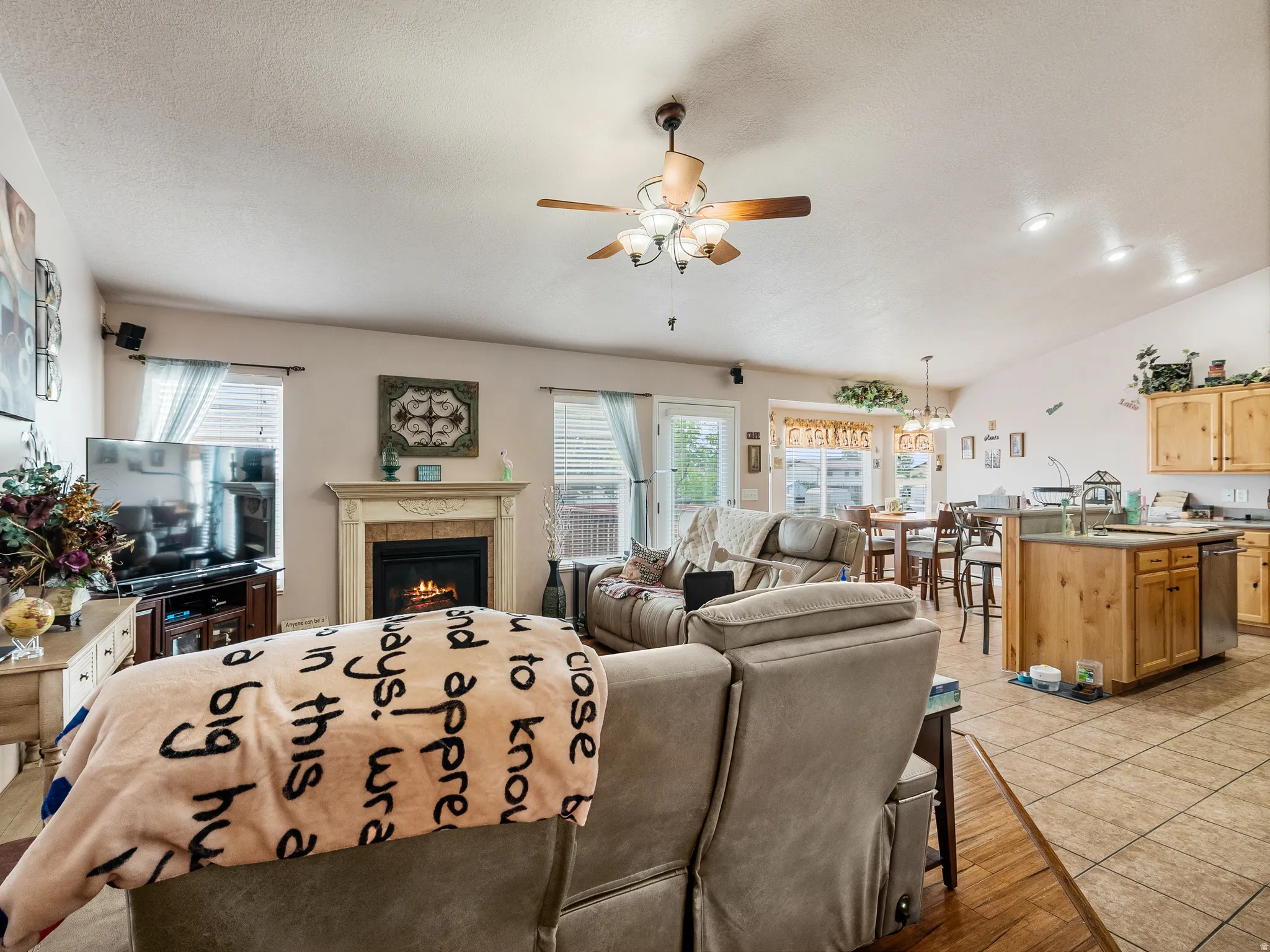Open-concept living space with a fireplace featuring a decorative mantel, wood-finish flooring, and a ceiling fan with light fixture