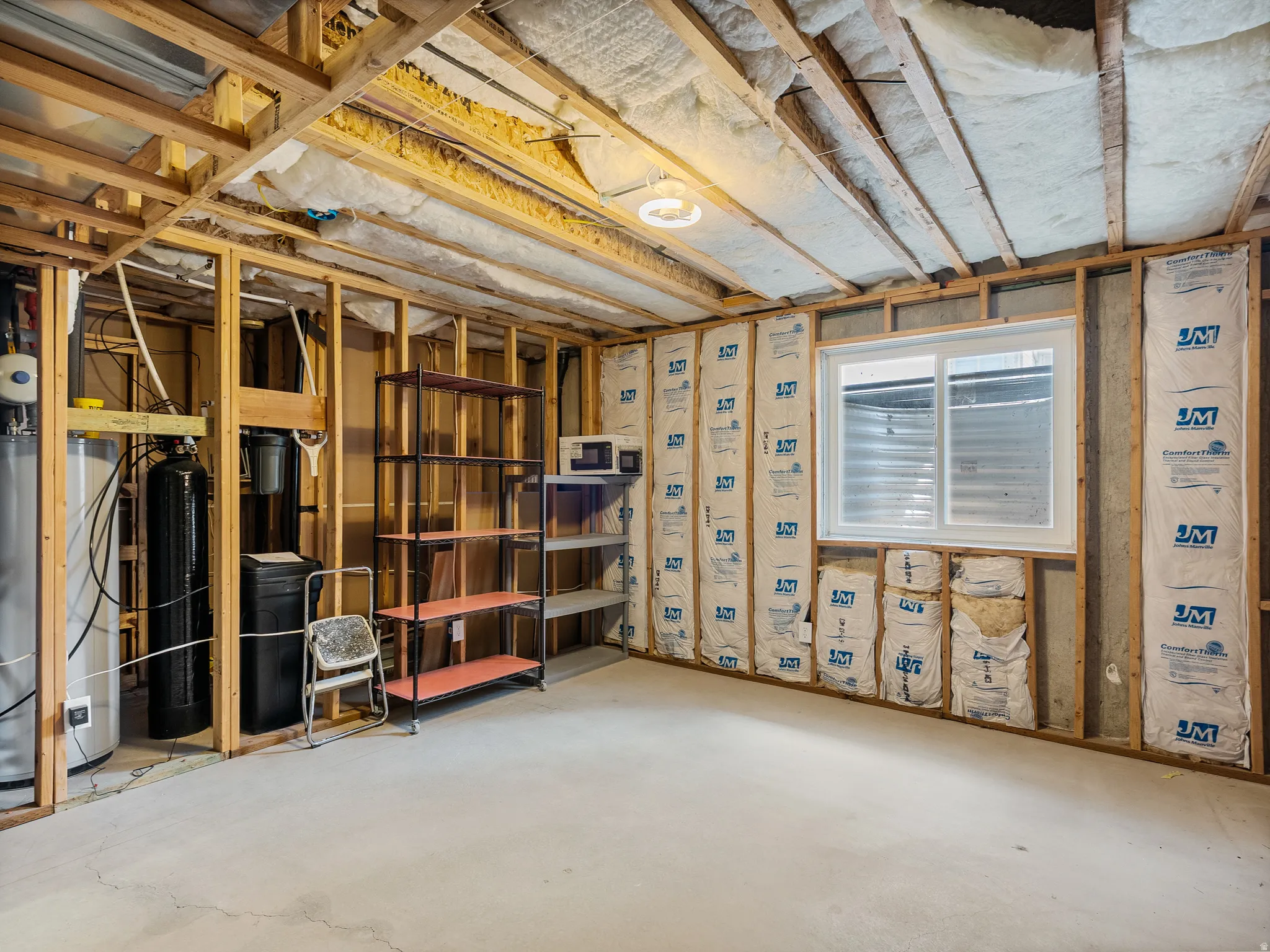 Unfinished basement featuring exposed wood framing, concrete flooring, and a large egress window