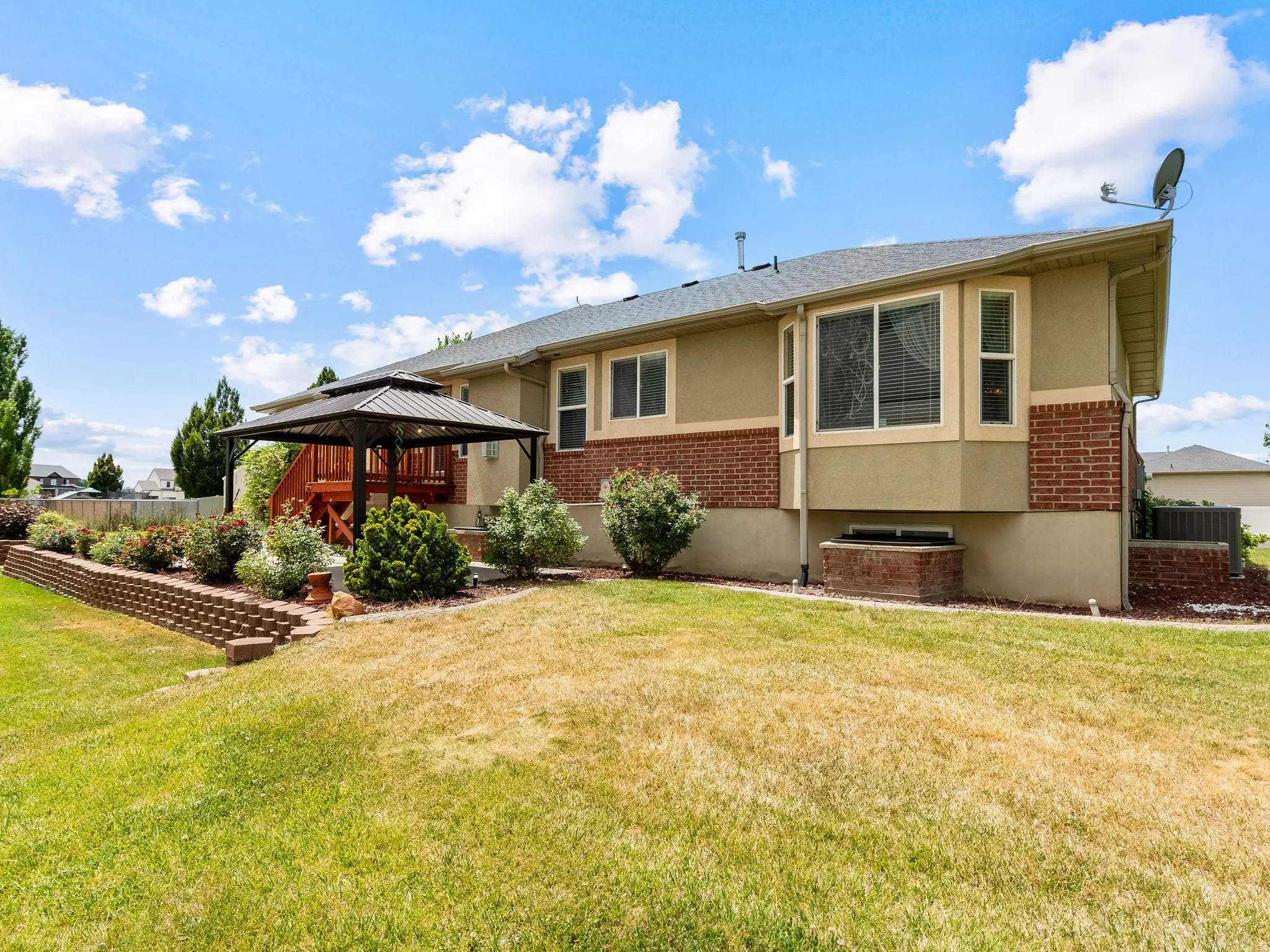 Rear exterior featuring a multi-level deck with a gazebo, mature landscaping, and a brick retaining wall