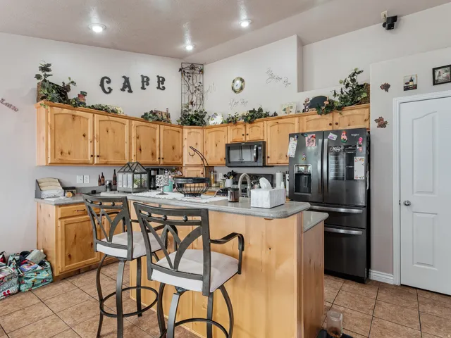 Kitchen featuring light wood cabinetry, stone-finish countertops, stainless steel appliances, and tile flooring