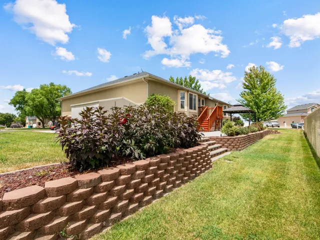Terraced landscaping featuring retaining walls, mature shrubs, a wooden deck with stairs, a stone patio, and a metal gazebo