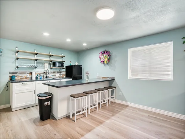 Kitchenette featuring light blue walls, wood-finish flooring, white cabinetry, open shelving, and a built-in countertop bar with seating