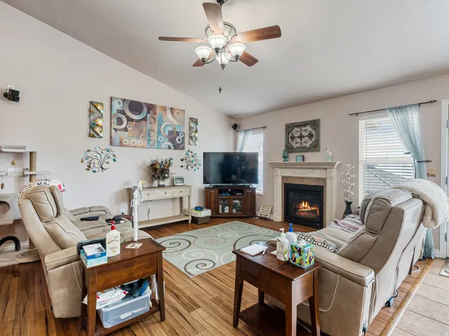 Living space featuring wood-finish flooring, a ceiling fan with integrated lighting, and a fireplace with a detailed mantel