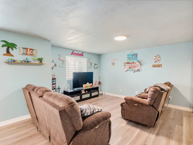 Living area featuring light wood-finish flooring, white baseboards, and a window with white louvered blinds