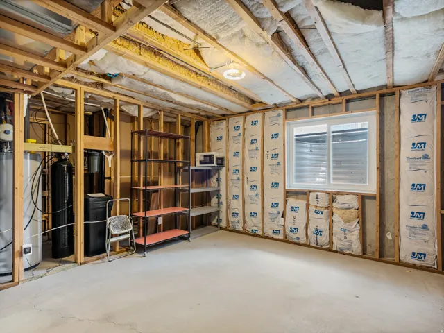 Unfinished basement featuring exposed wood framing, concrete flooring, and a large egress window